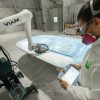 Man wearing PPE and holding a tablet operates a robotic sander.